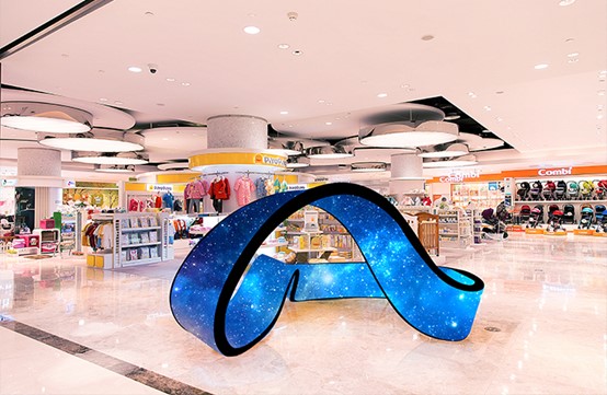 A large, blue Retop FC Series flexible LED screen display shaped like a curving ribbon, showing a galaxy pattern, located in the center of a bright shopping mall.
