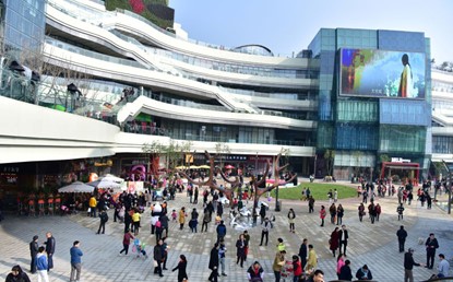 A large Retop TES II PRO outdoor LED billboard displaying an ad on the glass facade of a modern, multi-story shopping complex with a crowded plaza.